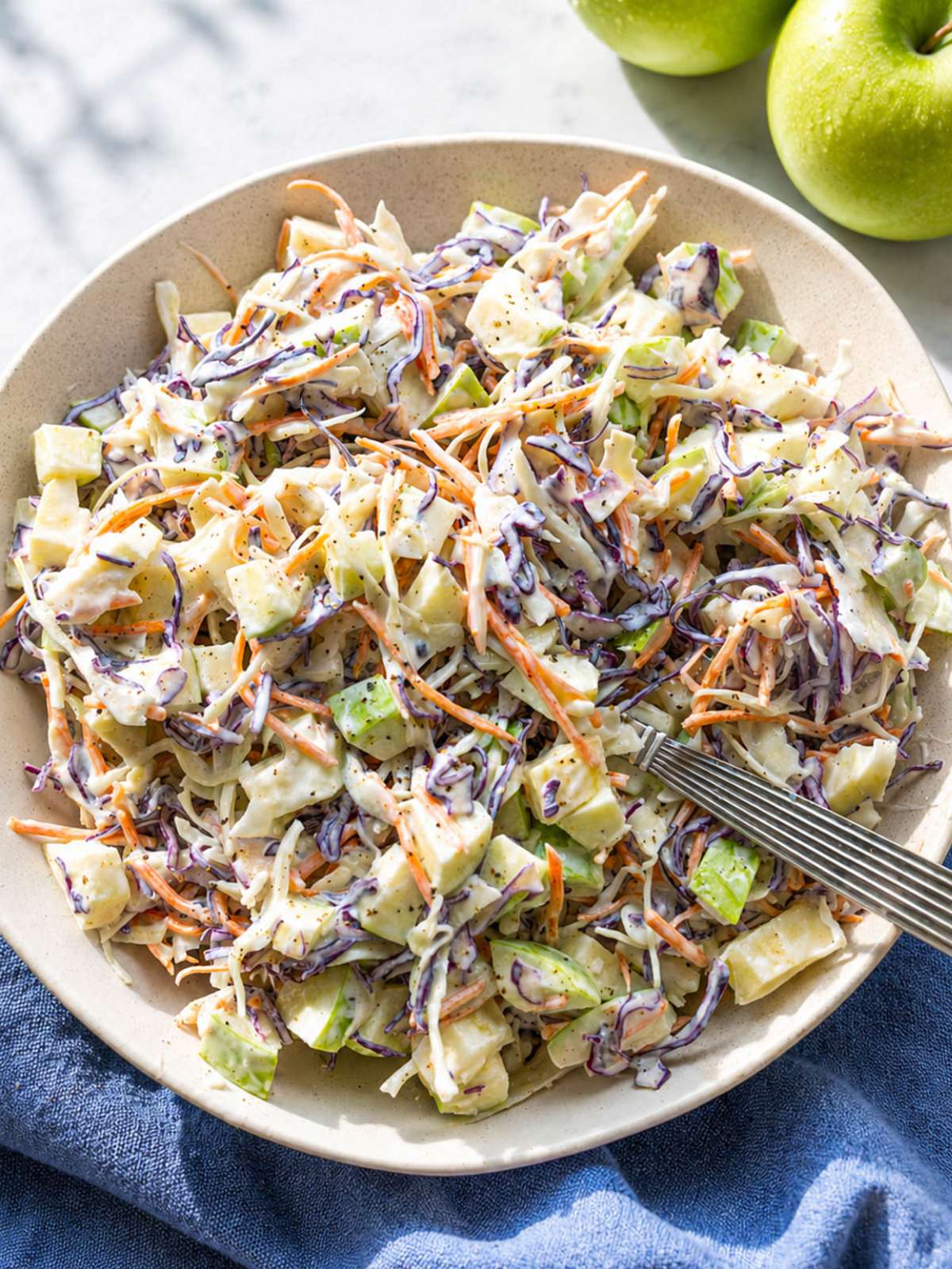 Creamy apple coleslaw in a serving bowl with fresh cabbage and crisp apple slices.