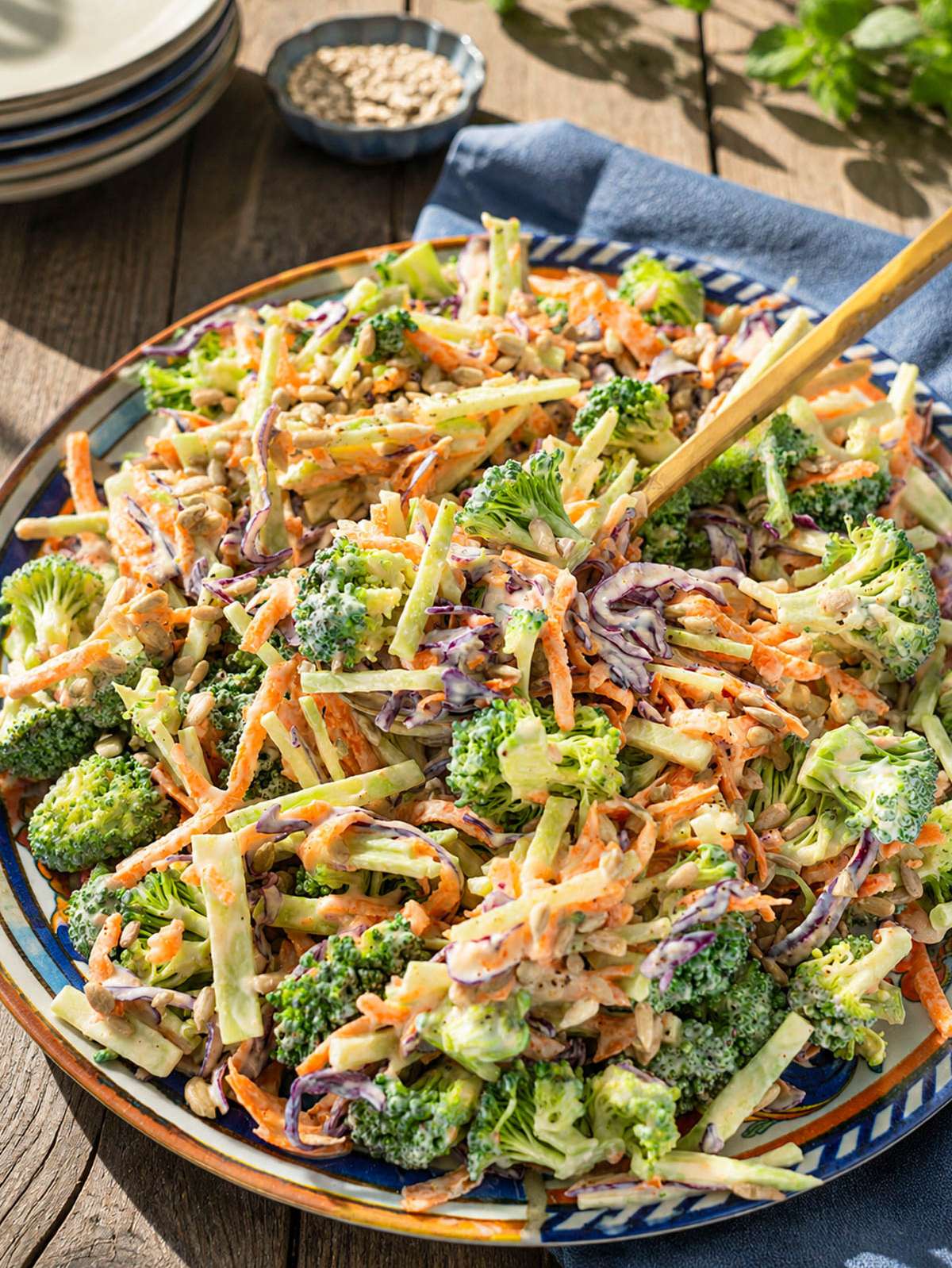 Creamy broccoli slaw with carrots, cabbage, and sunflower seeds served on a colorful platter.