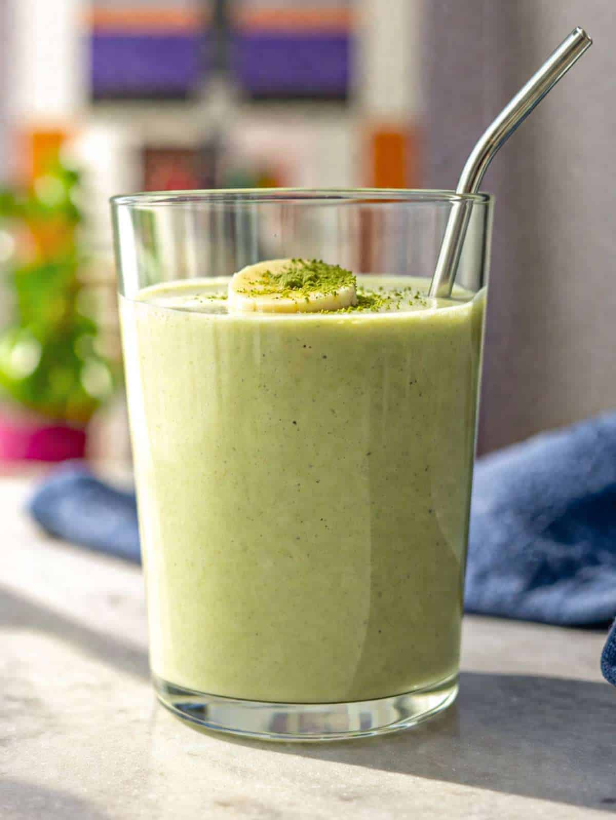 Creamy matcha smoothie in a glass on marble table with soft window light.