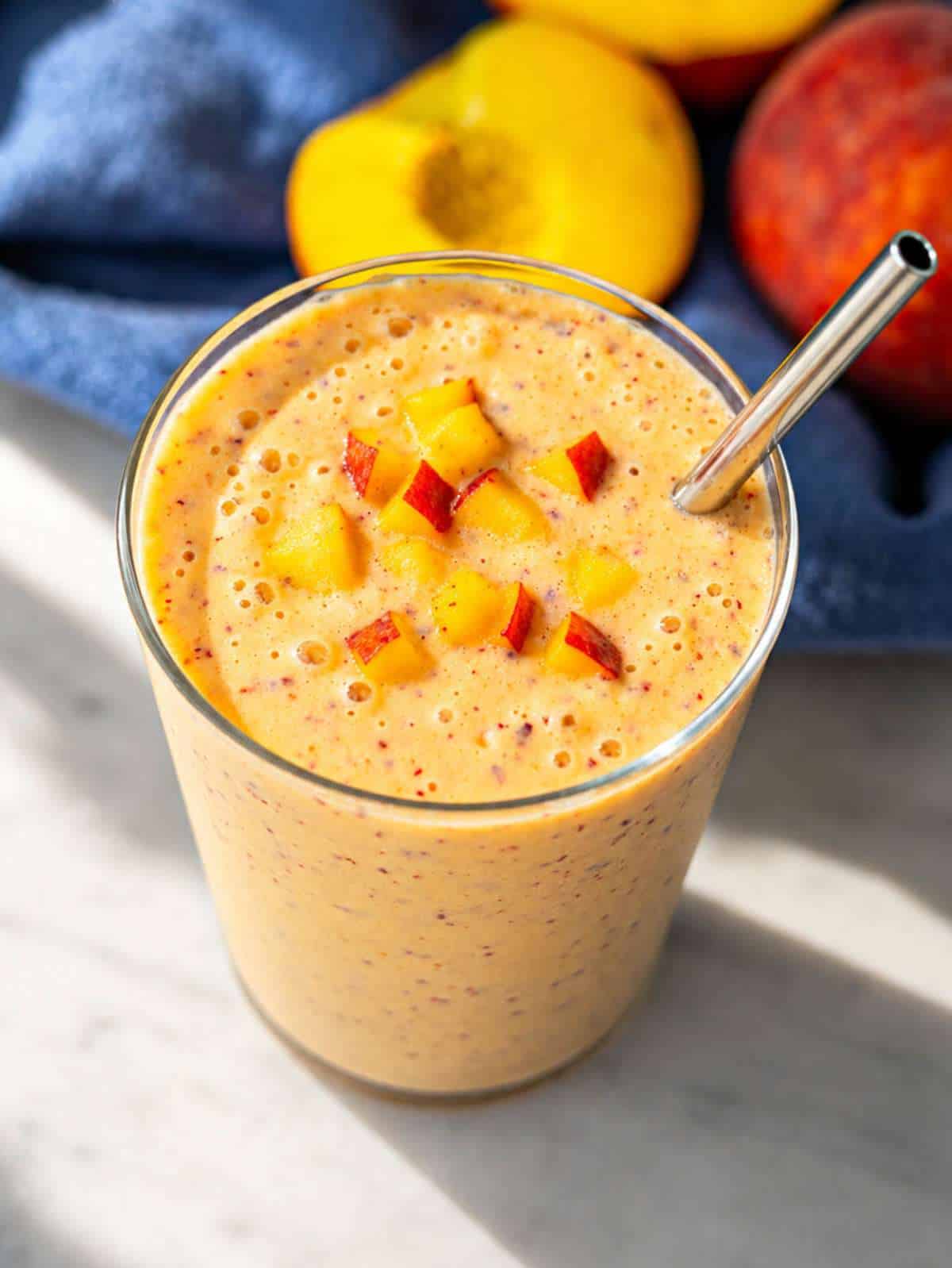 Creamy peach smoothie in a tall glass with peach slices and soft natural morning light.