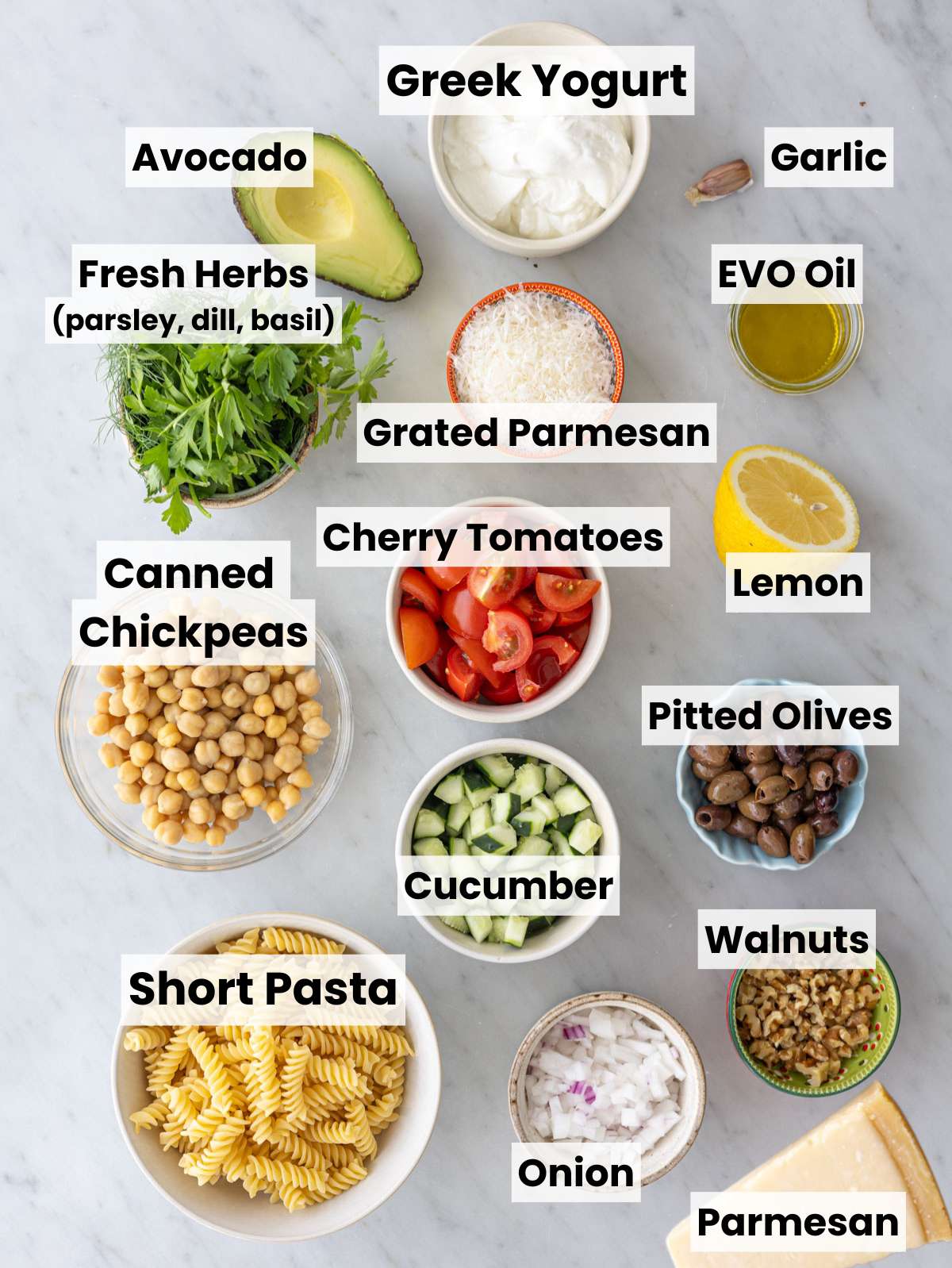 Fresh herbs, pasta, vegetables, and Greek yogurt arranged on marble table.