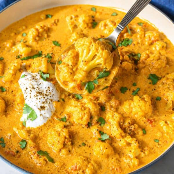 Greek yogurt cauliflower curry topped with herbs on white marble table in natural light.