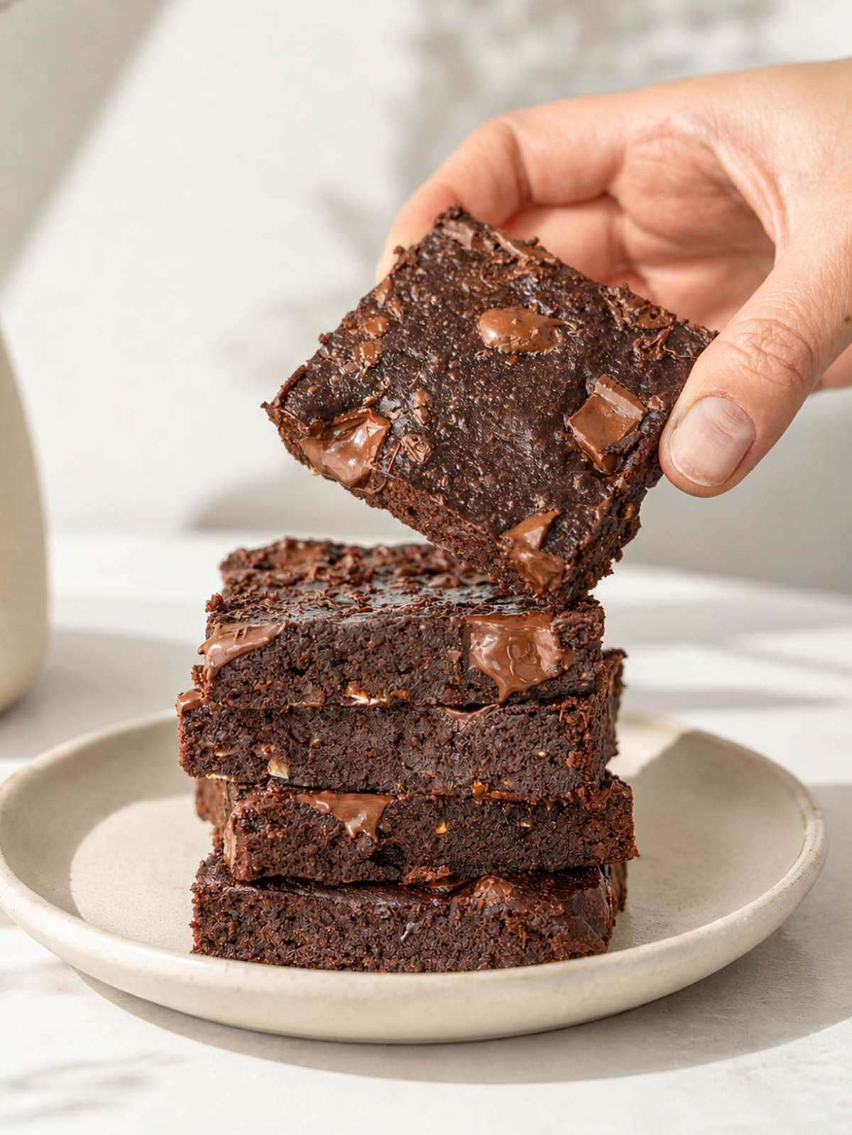 Hand lifting a rich chocolate date brownie from a stacked brownie tower.