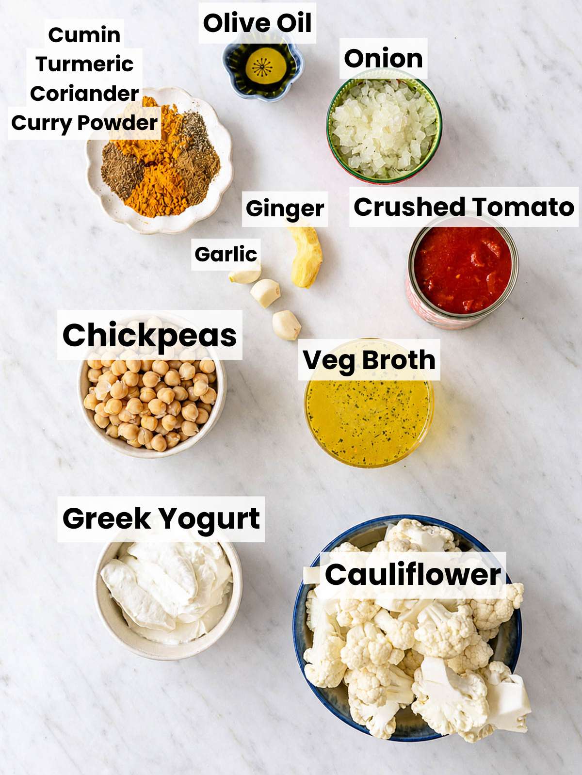 Ingredients for cauliflower curry arranged on white marble counter near a bright kitchen window.