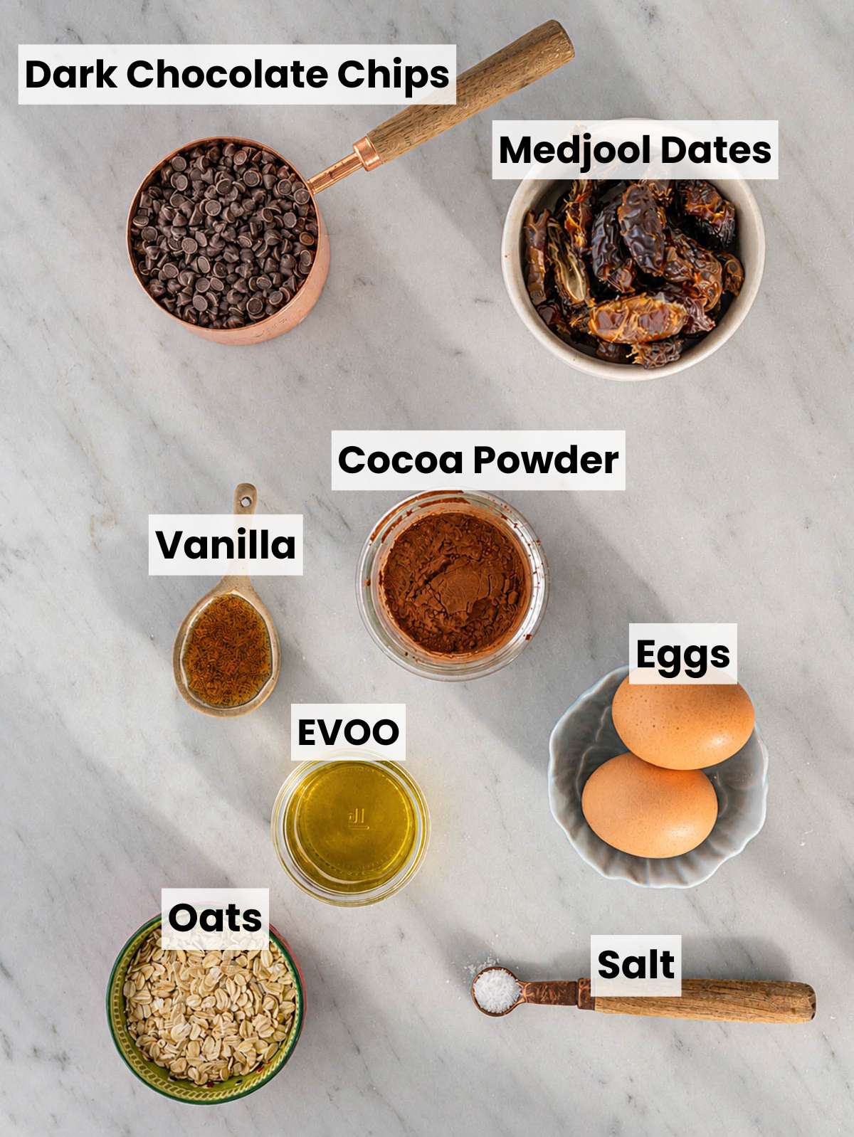 Medjool dates, oats, cocoa, eggs, olive oil, and chocolate on marble.