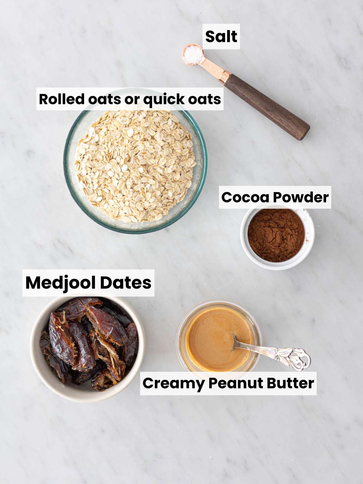Medjool dates, oats, peanut butter, cocoa powder, and salt on white marble counter.