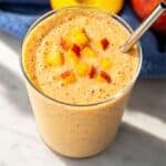 Peach smoothie served in a chilled glass on white marble.