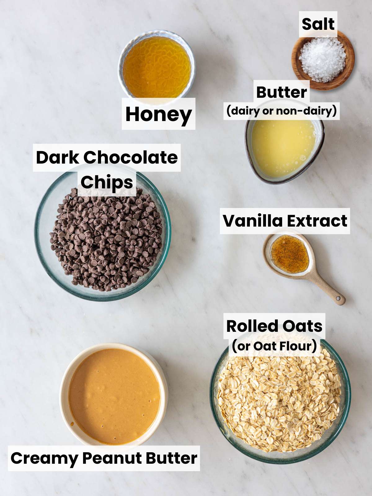 Peanut butter, oats, honey, chocolate chips, and butter on marble countertop.