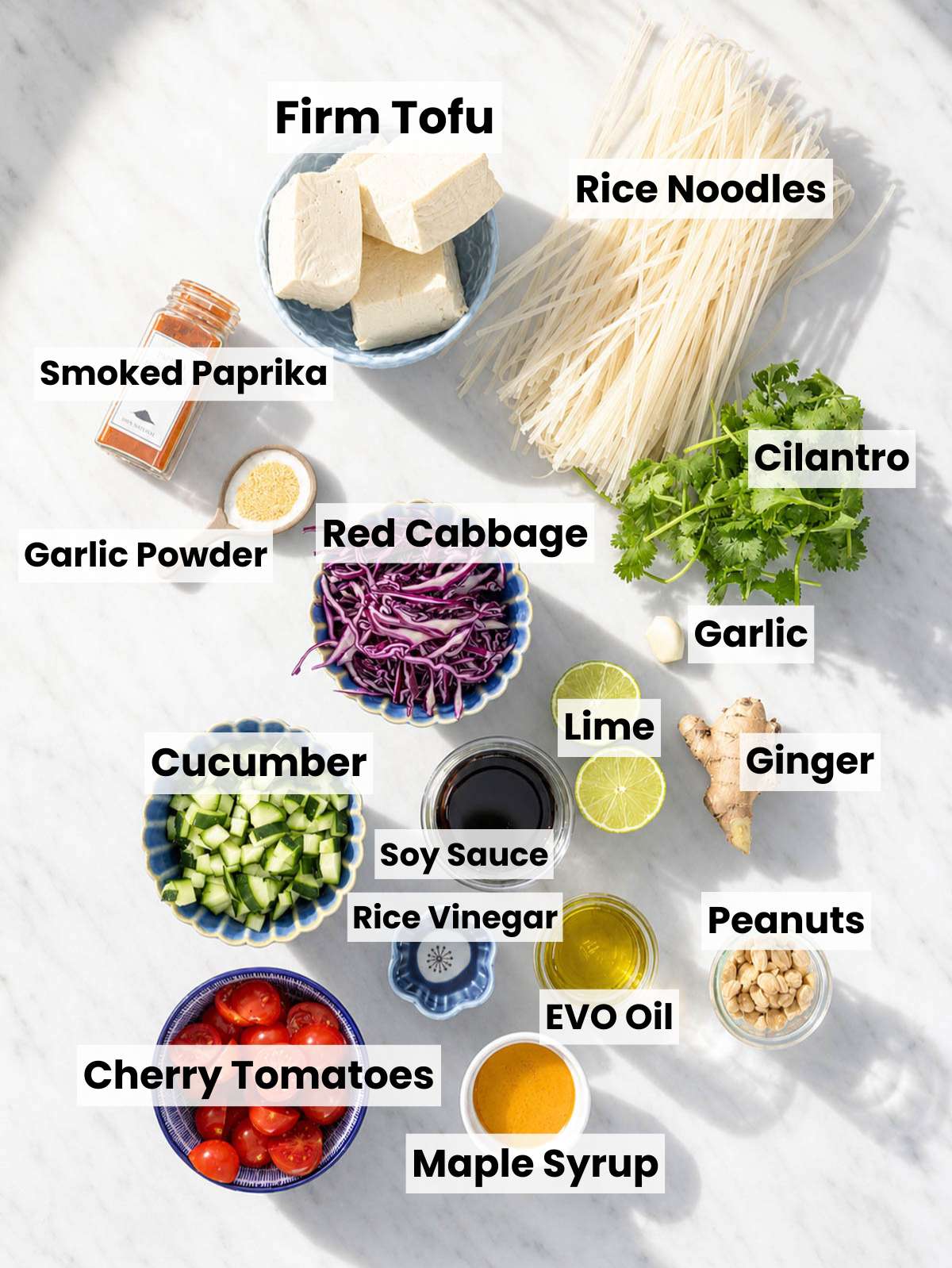 Rice noodles, tofu, cabbage, cucumber, and tomatoes on a marble counter.