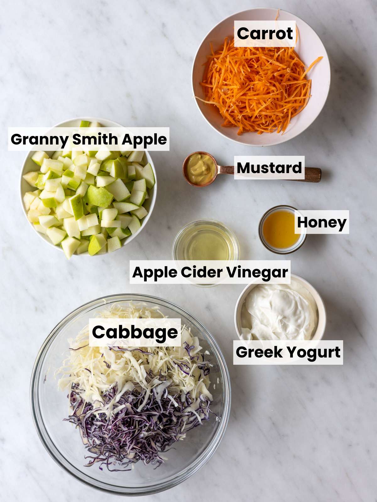 Shredded cabbage, apples, carrots, green onions, yogurt, mustard, and vinegar on marble countertop.