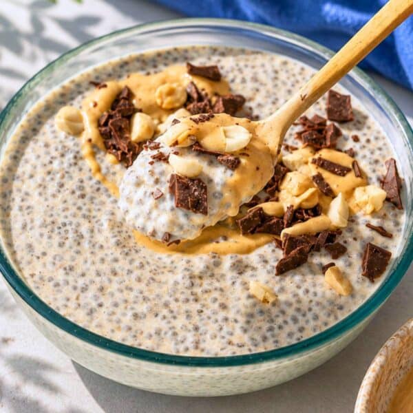 Spoon lifting creamy peanut butter chia pudding topped with dark chocolate and crushed peanuts