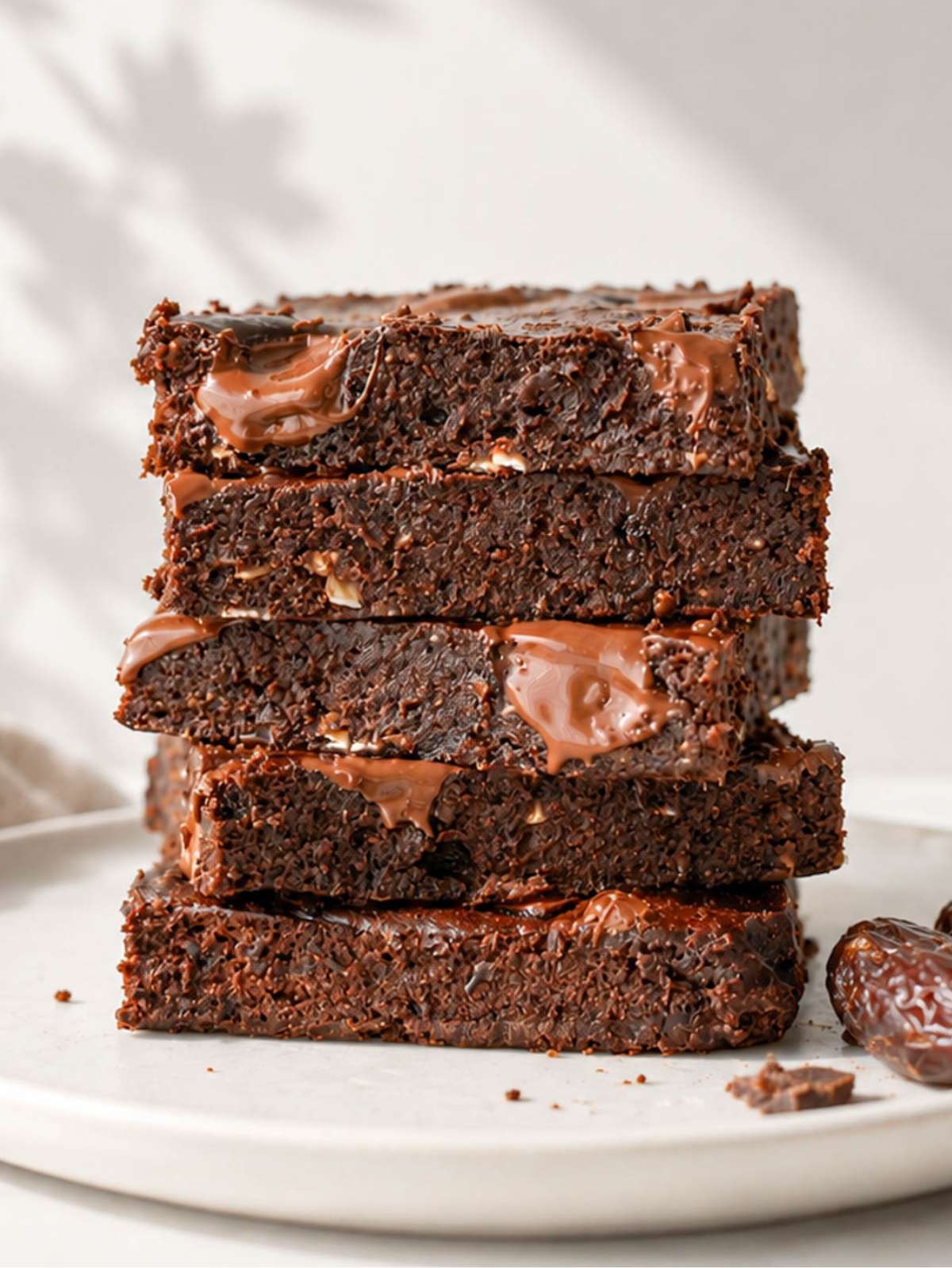 Stack of fudgy date brownies with melted chocolate chunks on a ceramic plate.