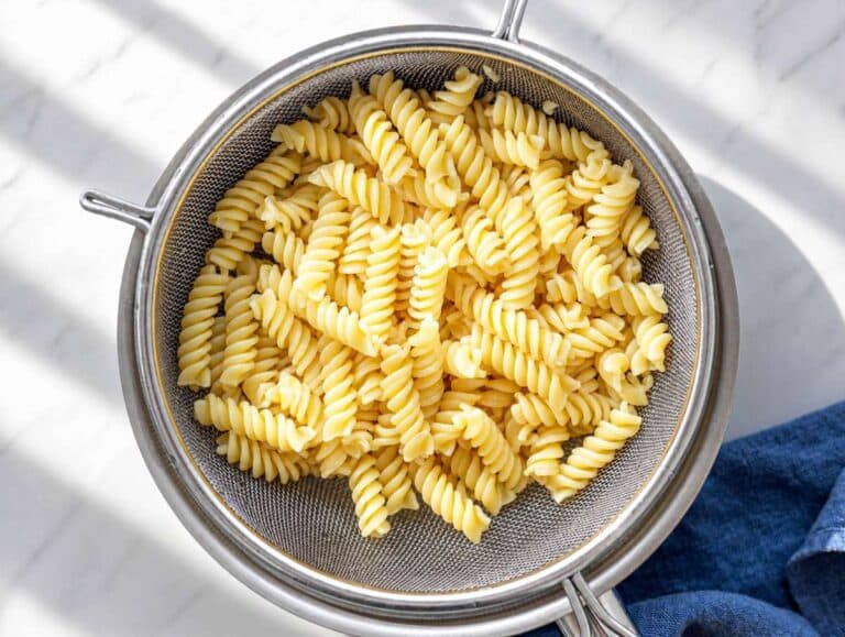 Step 1 Boiled pasta draining in colander with steam rising in natural window light.
