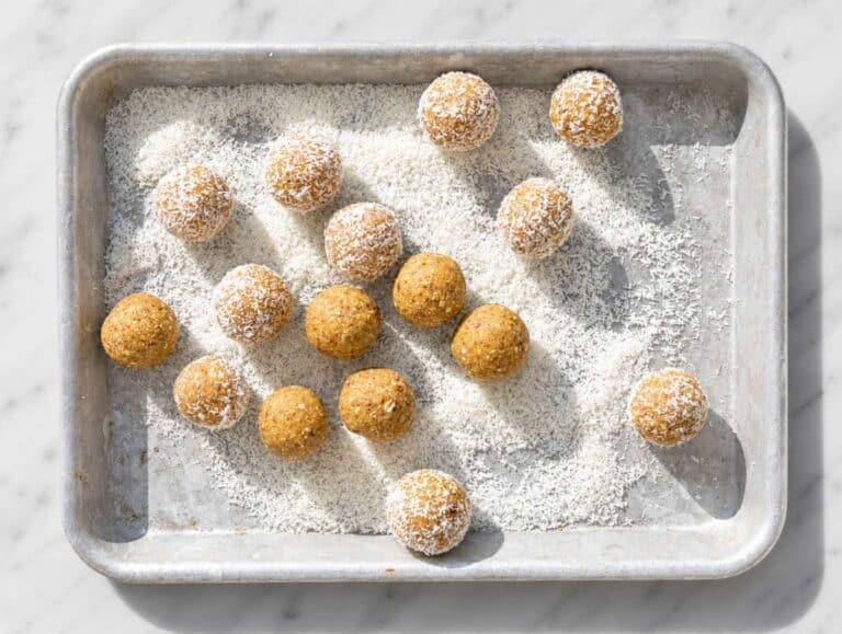 Step 2 Coconut-coated lemon energy bites resting on baking tray with scattered shredded coconut.