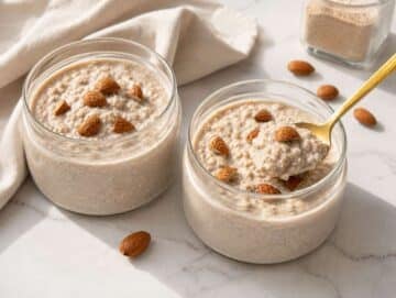 Step 3 Two jars of creamy protein overnight oats topped with almonds on a bright marble counter.