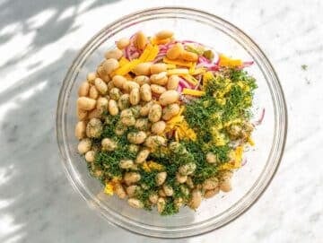 Step 3 White bean salad with cheddar, dill, and red onion in glass bowl on marble counter.