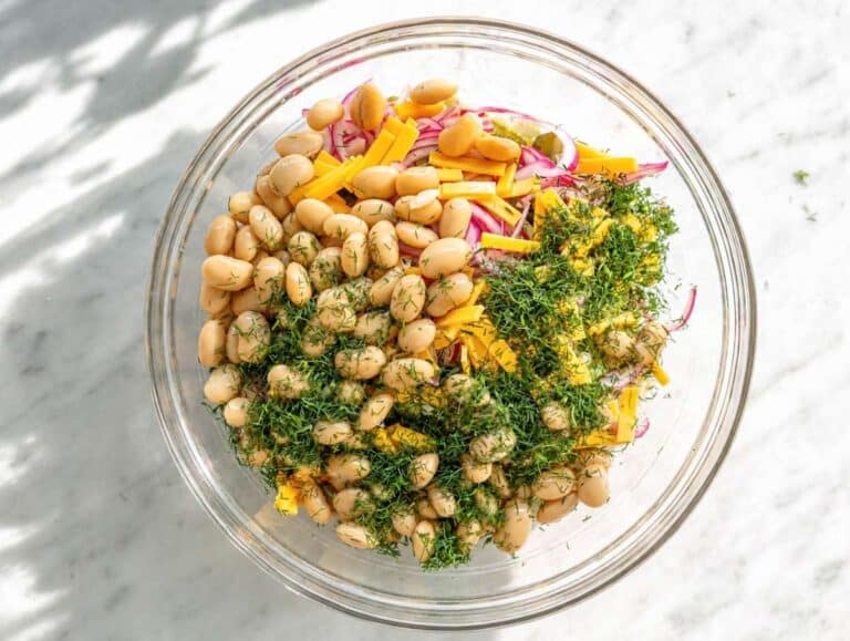 Step 3 White bean salad with cheddar, dill, and red onion in glass bowl on marble counter.