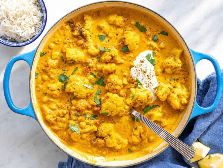 Step 5 Cauliflower curry served with basmati rice, herbs, and lemon wedges on marble table.