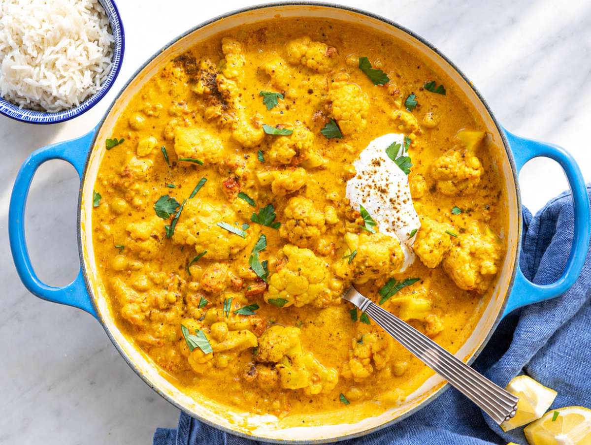 Step 5 Cauliflower curry served with basmati rice, herbs, and lemon wedges on marble table.