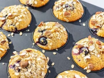 Step 5 Golden blueberry protein muffins cooling in the muffin pan on a marble surface.