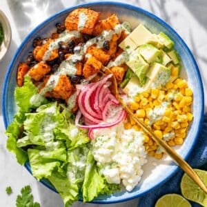 Sweet potato black bean bowl served with fresh toppings on a white marble table.