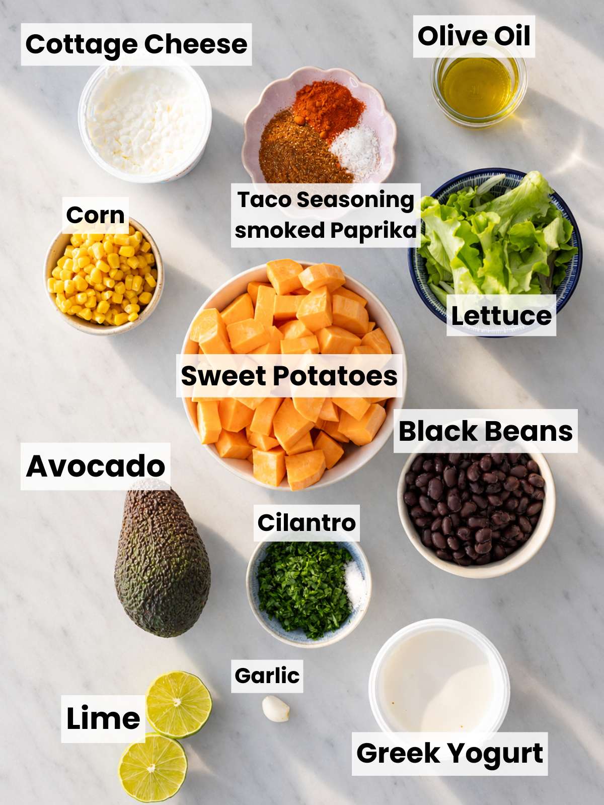 Sweet potatoes, black beans, lettuce, avocado, lime, and spices on a marble countertop.