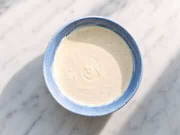 step 2 Whisking creamy Greek yogurt dill pickle dressing in small white bowl.