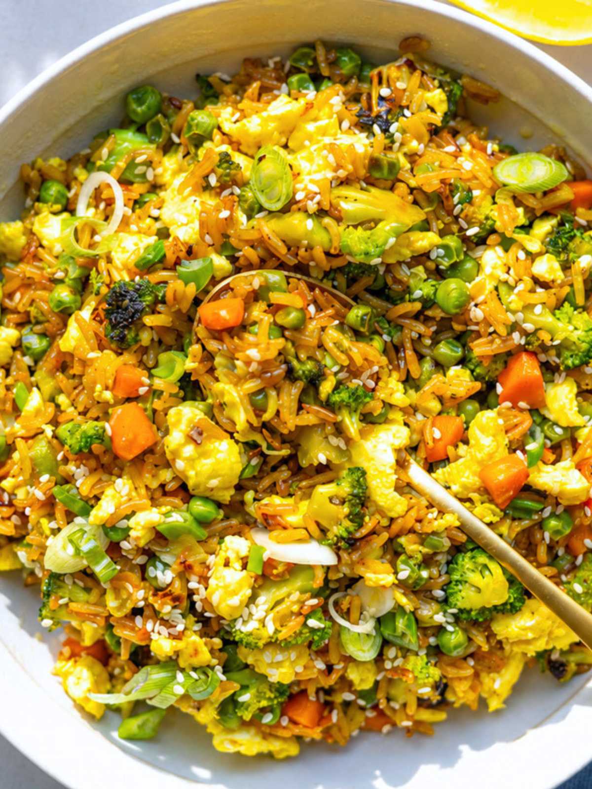 Bowl of vegetable fried rice with broccoli, peas, carrots, scallions, and fluffy scrambled eggs.