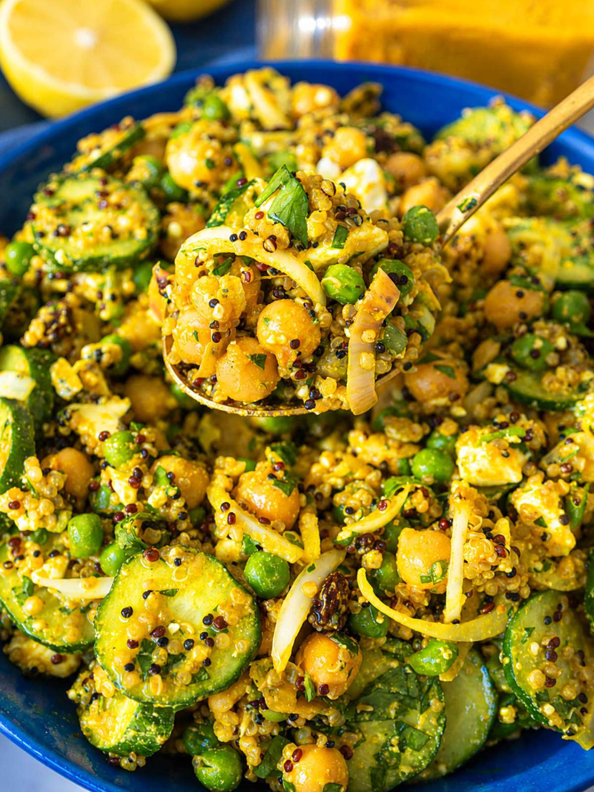 Close-up of glossy turmeric chickpeas with quinoa, feta, peas, and cucumber.