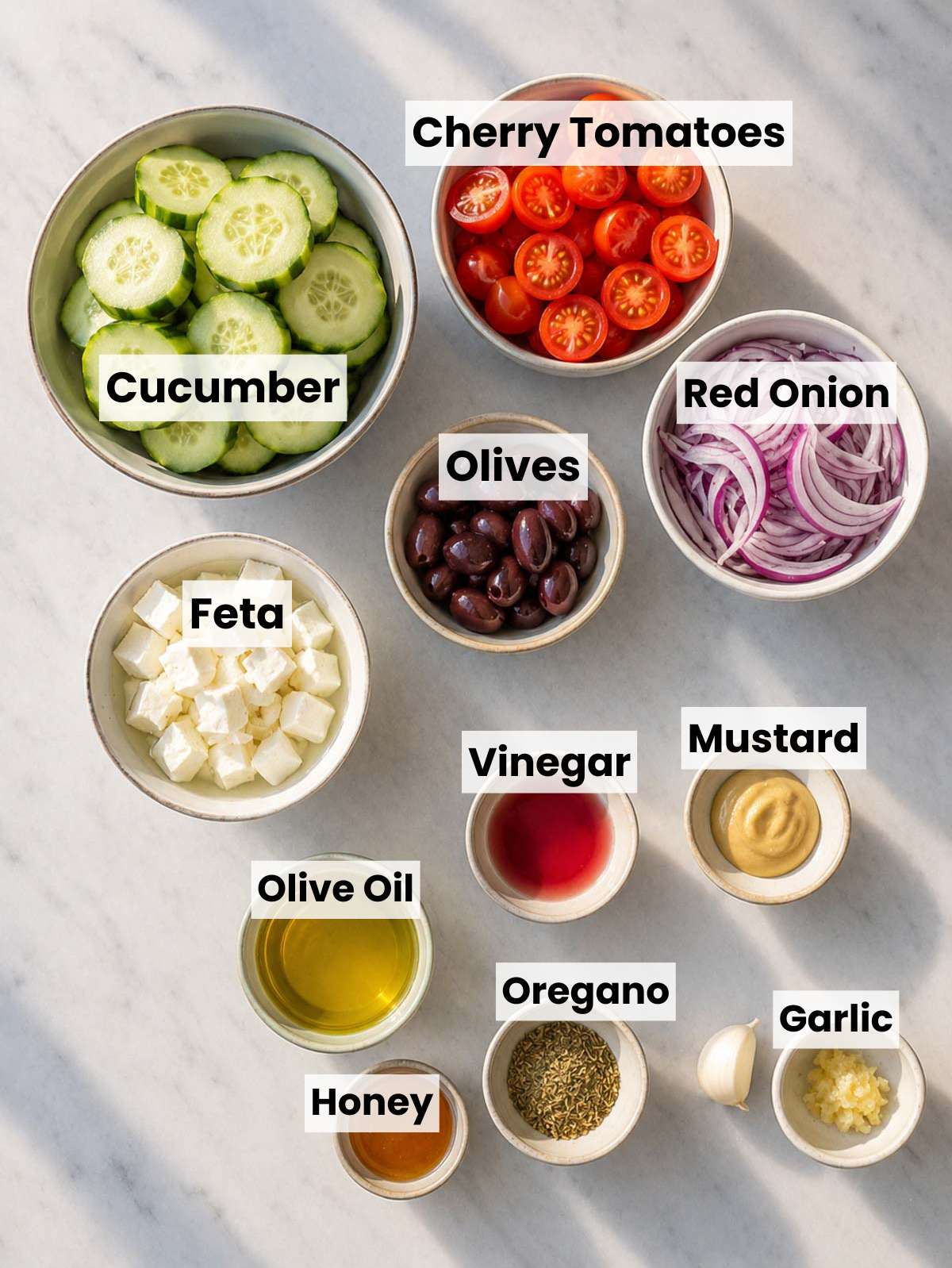 Ingredients for Greek cucumber salad with cucumbers, tomatoes, feta, olives, red onion, and herbs on marble.