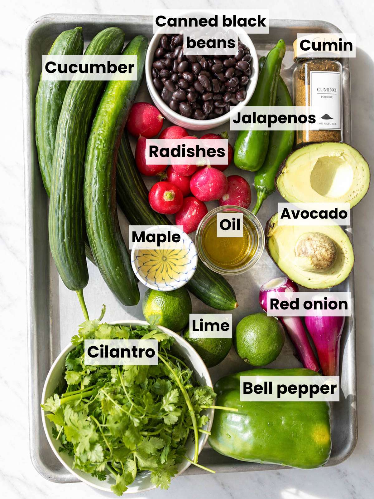 Ingredients for Mexican cucumber salad arranged on white marble in natural light.