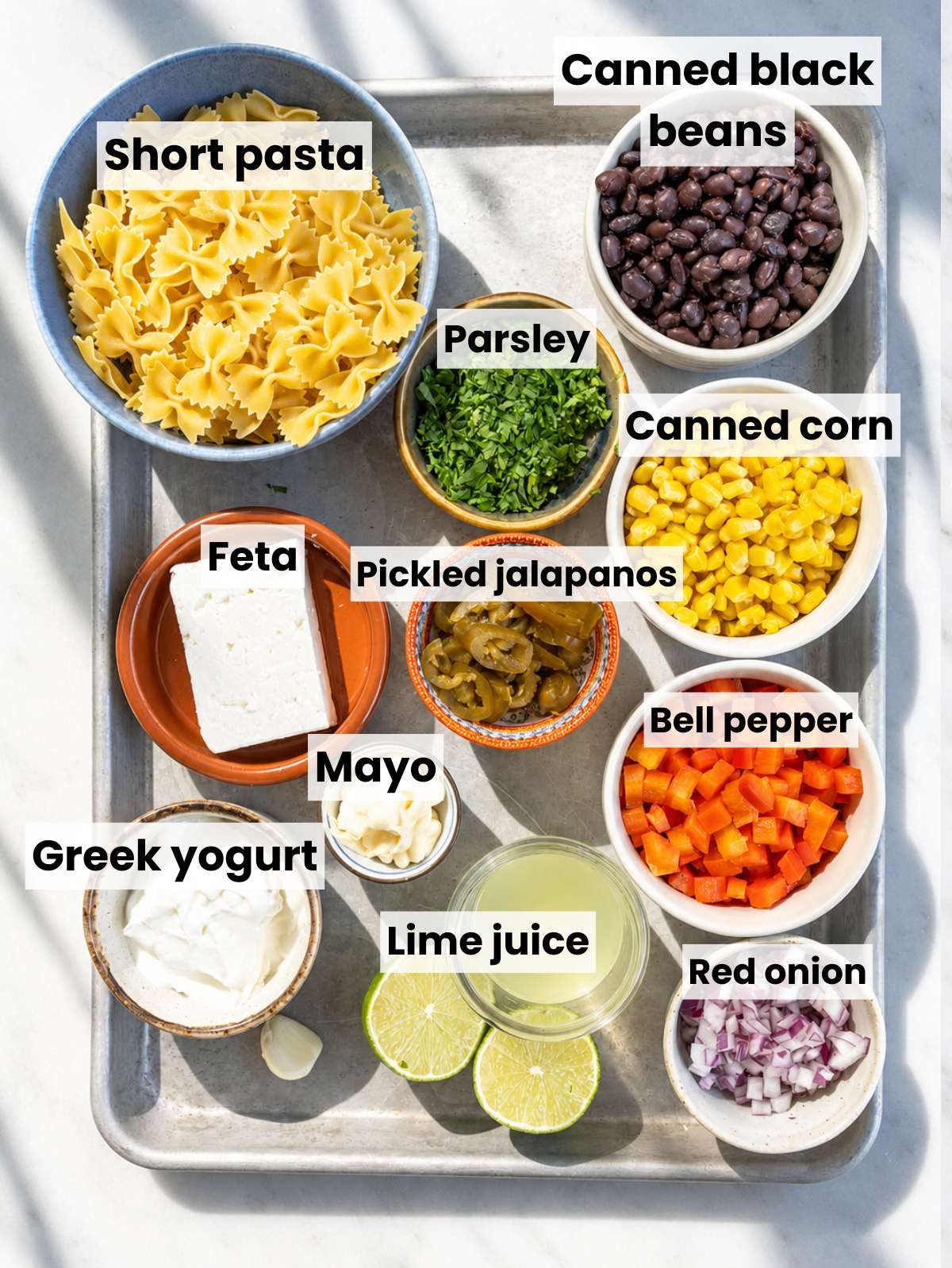Ingredients for Mexican pasta salad arranged in bowls on a white marble countertop.