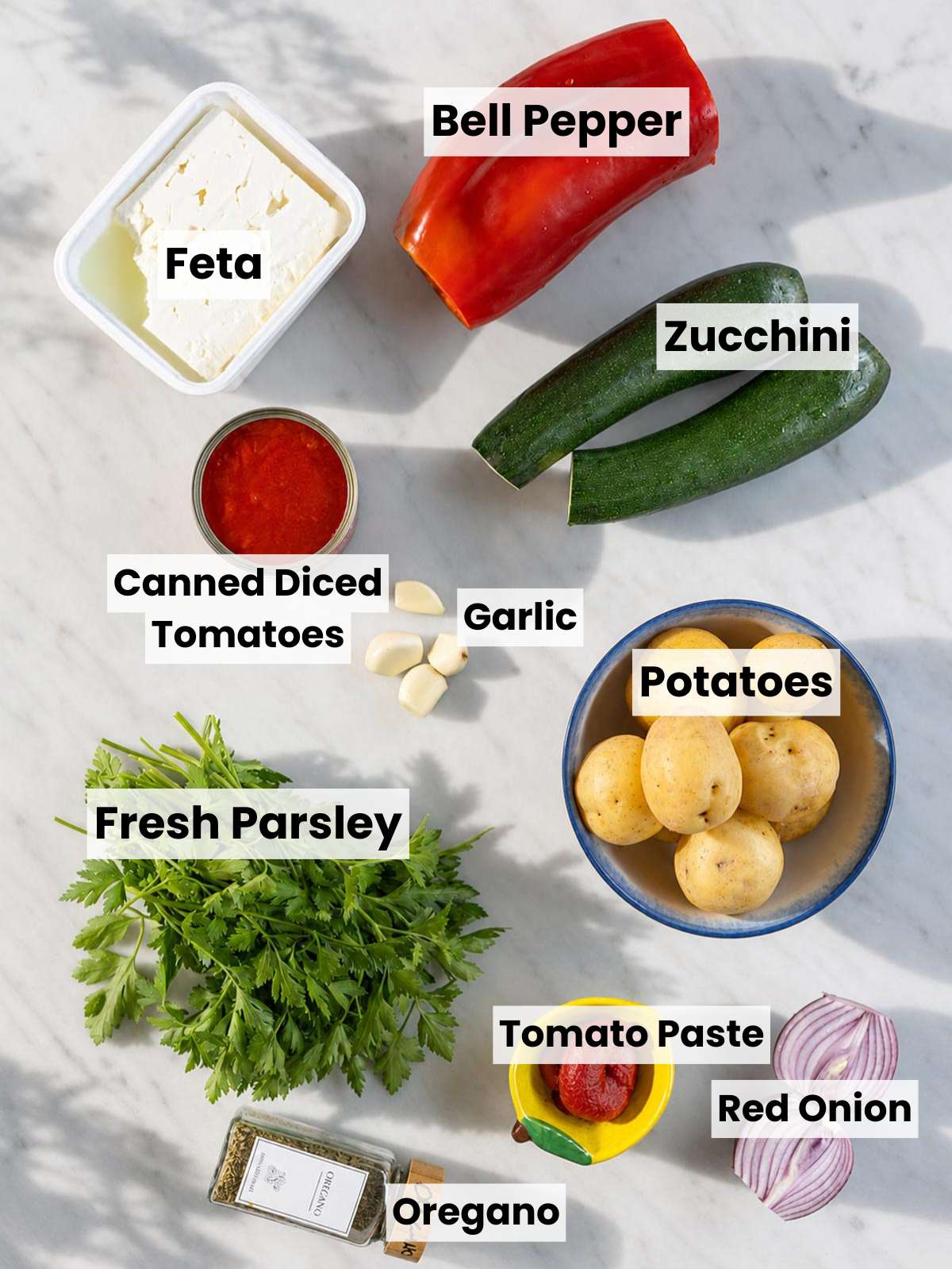 Ingredients for briam arranged on a marble countertop in natural window light.