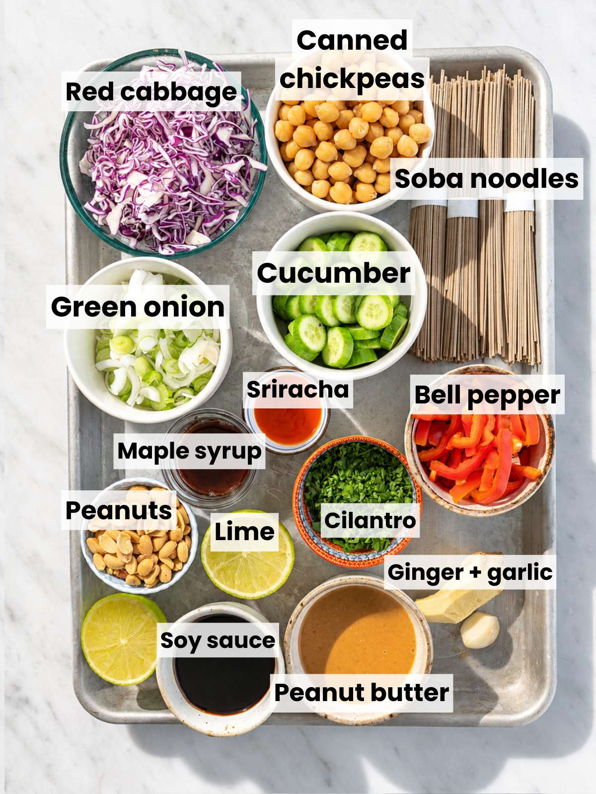 Ingredients for soba noodle salad arranged in bowls on marble counter.