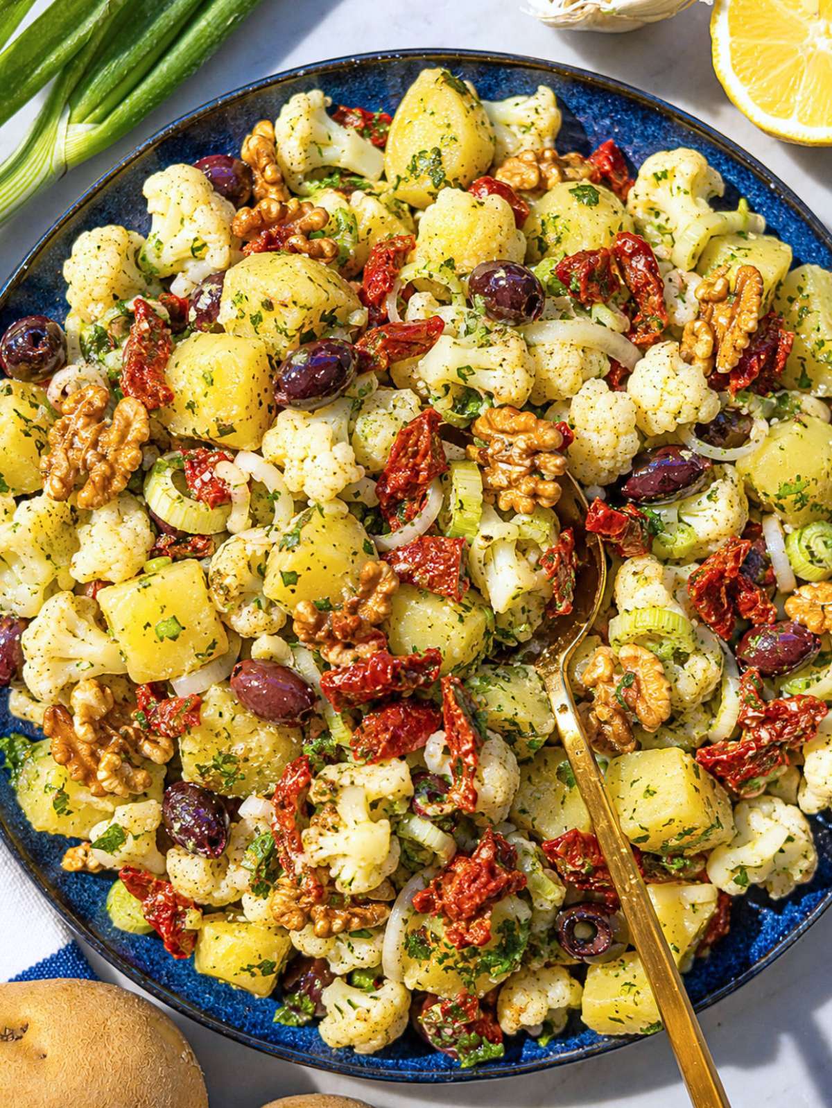 Potato cauliflower salad with olives, walnuts, and parsley in a large serving bowl.