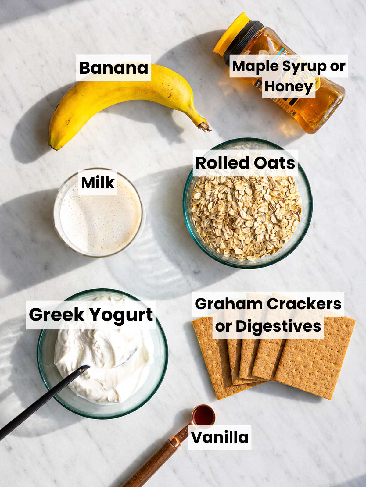 Rolled oats, banana, Greek yogurt, vanilla, wafers arranged on table.