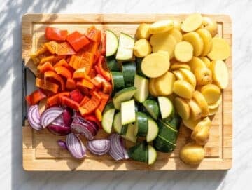 Step 1 Sliced potatoes, zucchini, peppers, and onions on a marble countertop.
