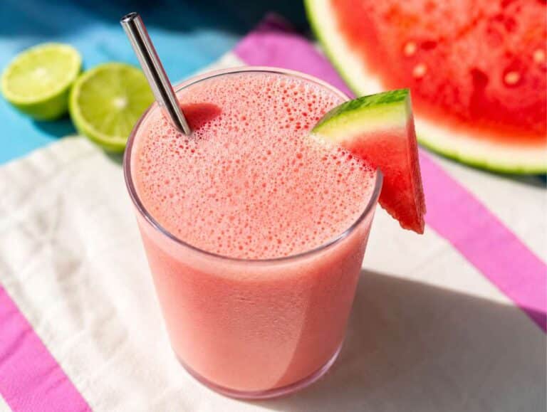 Watermelon smoothie poured into a glass beside fresh lime.