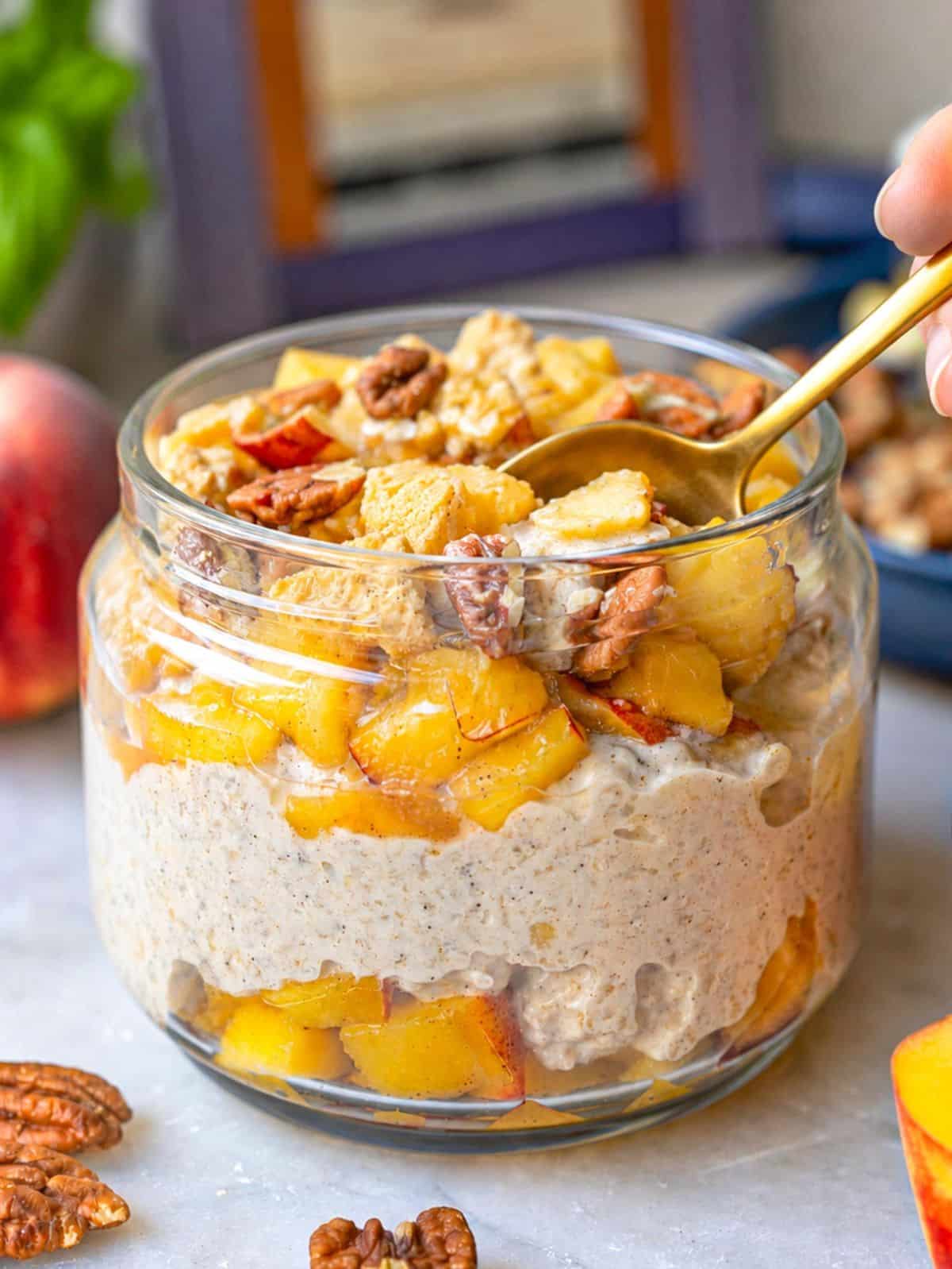 overnight oats topped with peaches, yogurt, pecans and with a spoon.