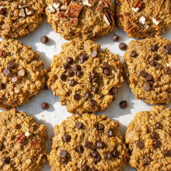Banana peanut butter cookies with chocolate chips and pecans on parchment in bright daylight.