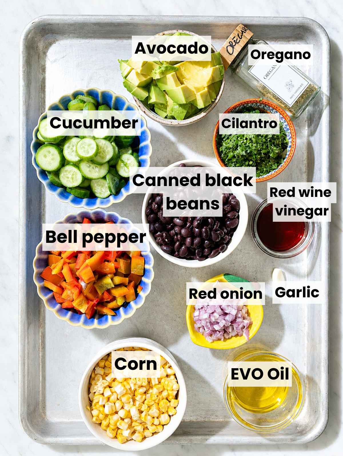 Black beans, vegetables, herbs, and dressing ingredients on white Carrara marble countertop.