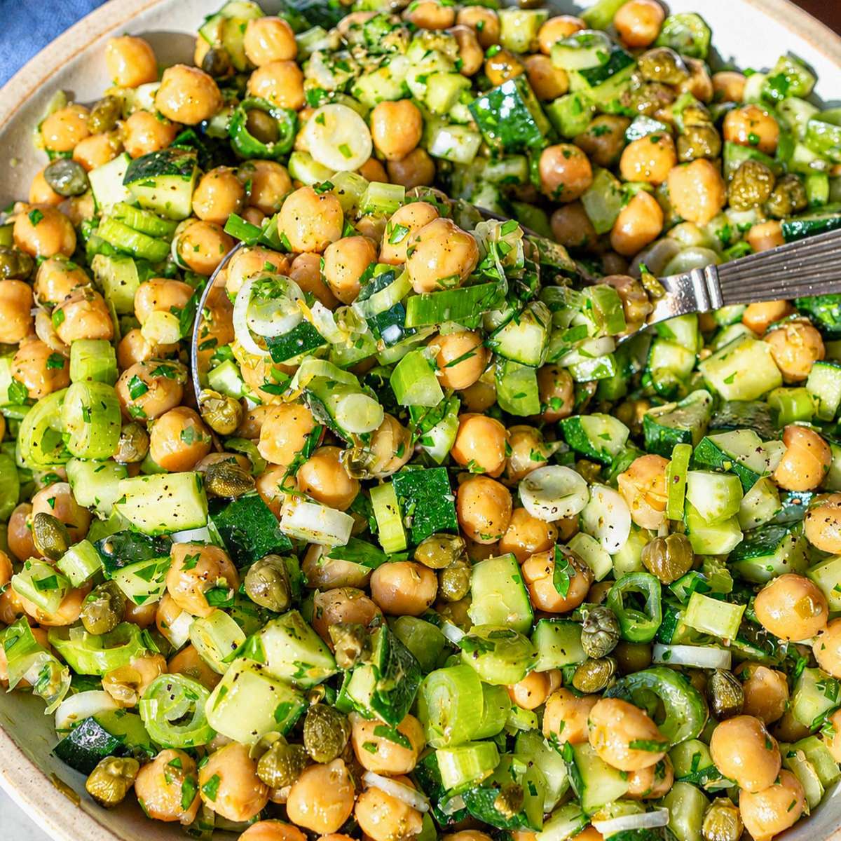 Bowl of Piccata Chickpea Salad with lemon dressing in white bowl.