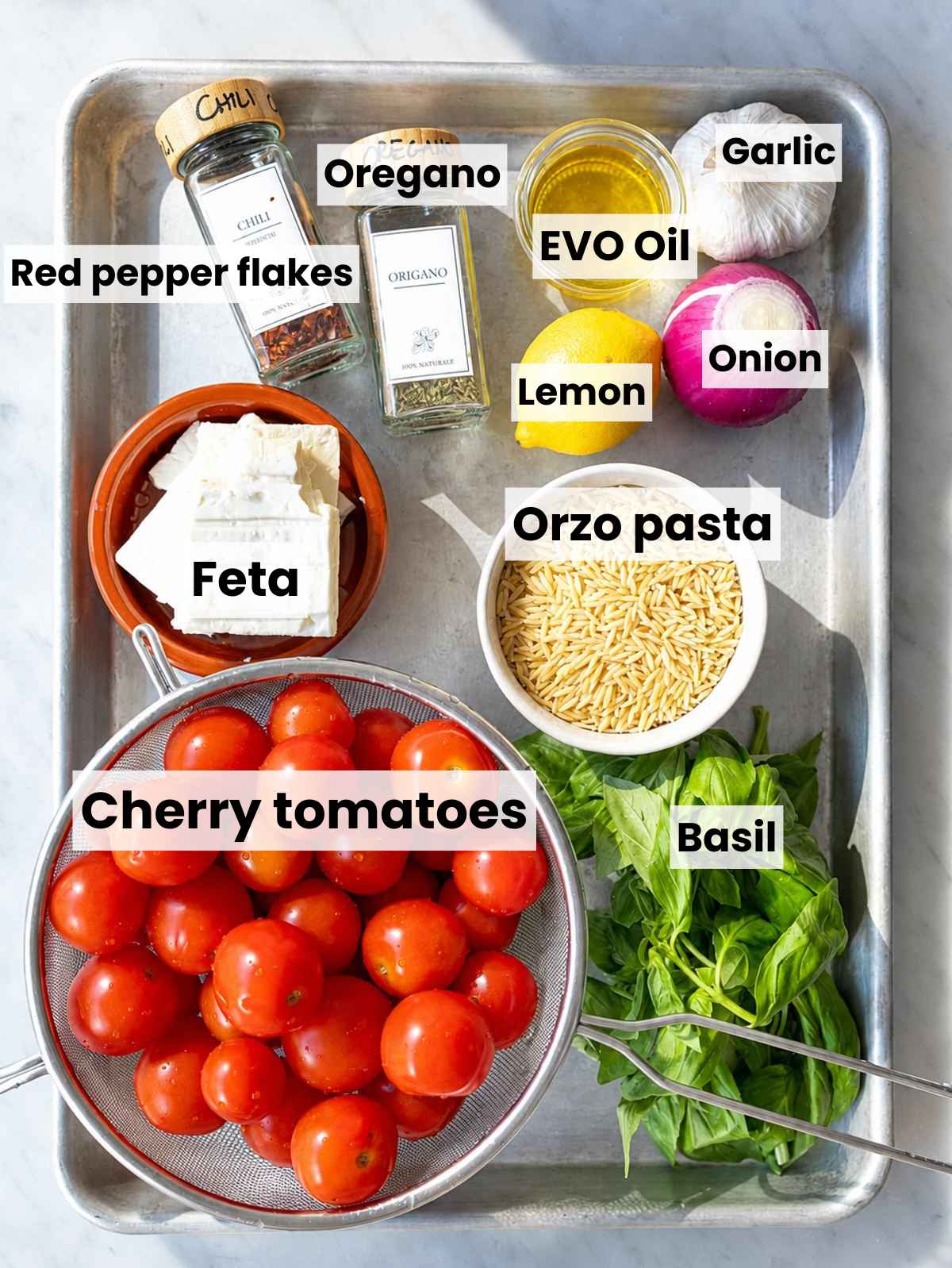 Cherry tomatoes, orzo, feta, onion, garlic, basil, lemon, olive oil, seasonings on marble.
