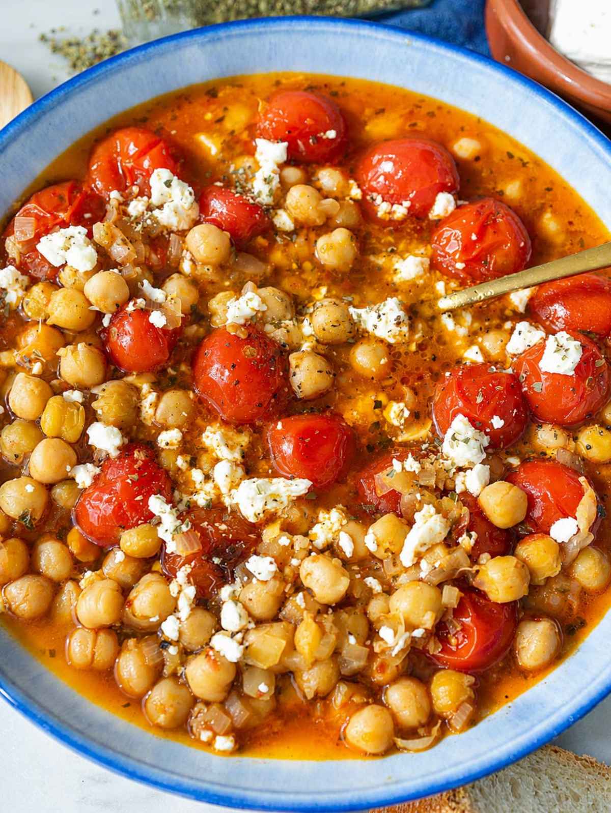Close-up of glossy chickpeas, burst tomatoes, creamy feta, and oregano.