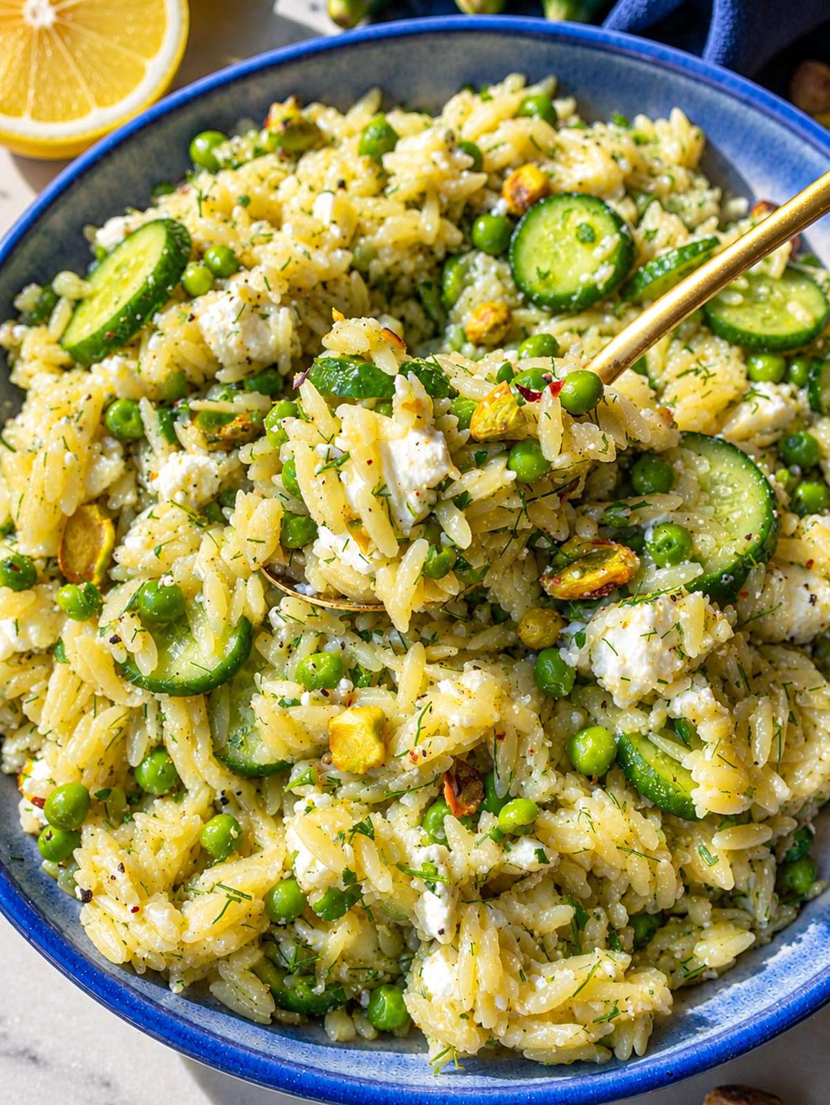 Close-up of glossy lemon orzo salad with creamy feta and fresh herbs.