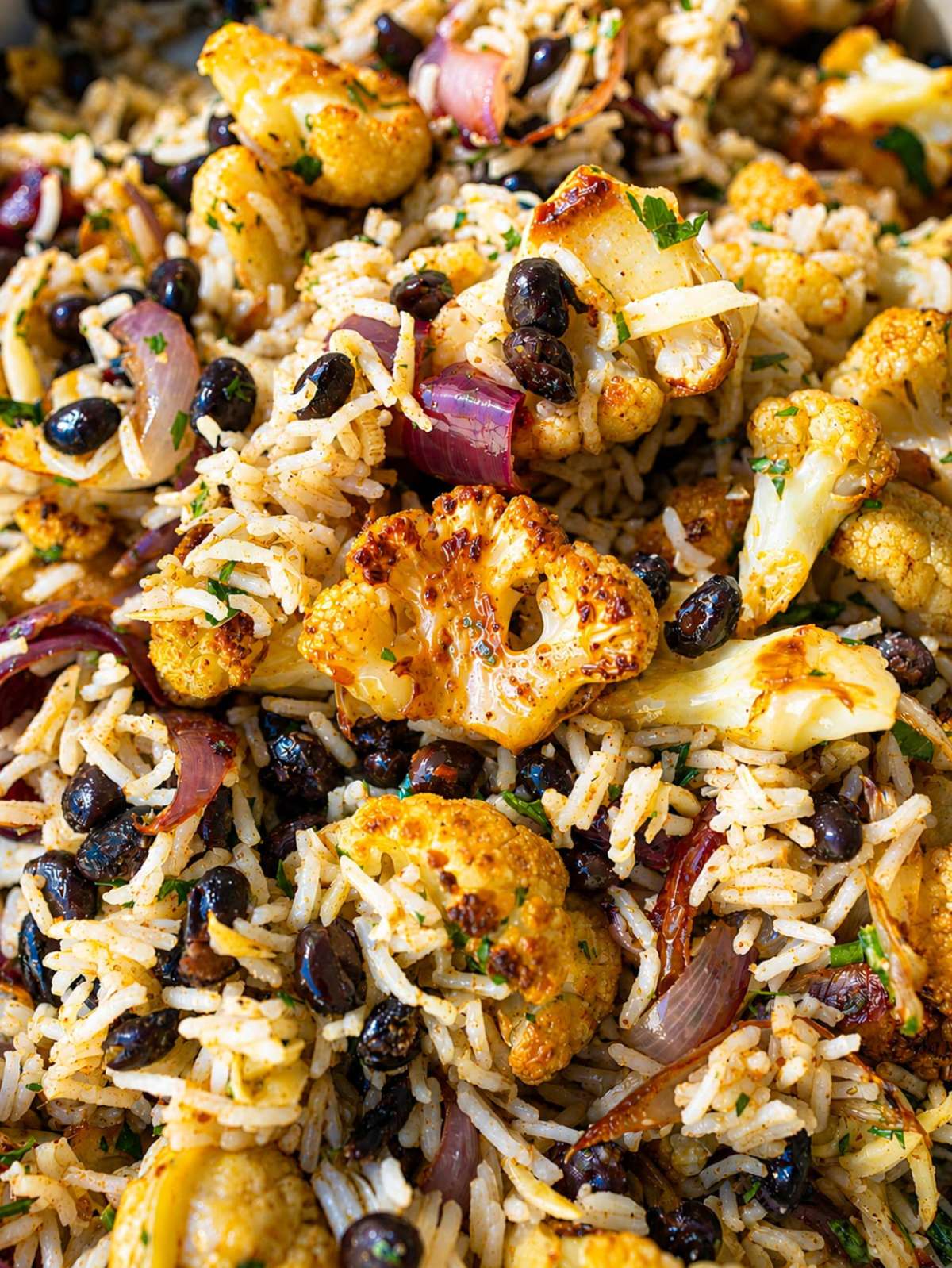 Close-up of glossy roasted cauliflower, fluffy rice, black beans, red onion, and herbs.