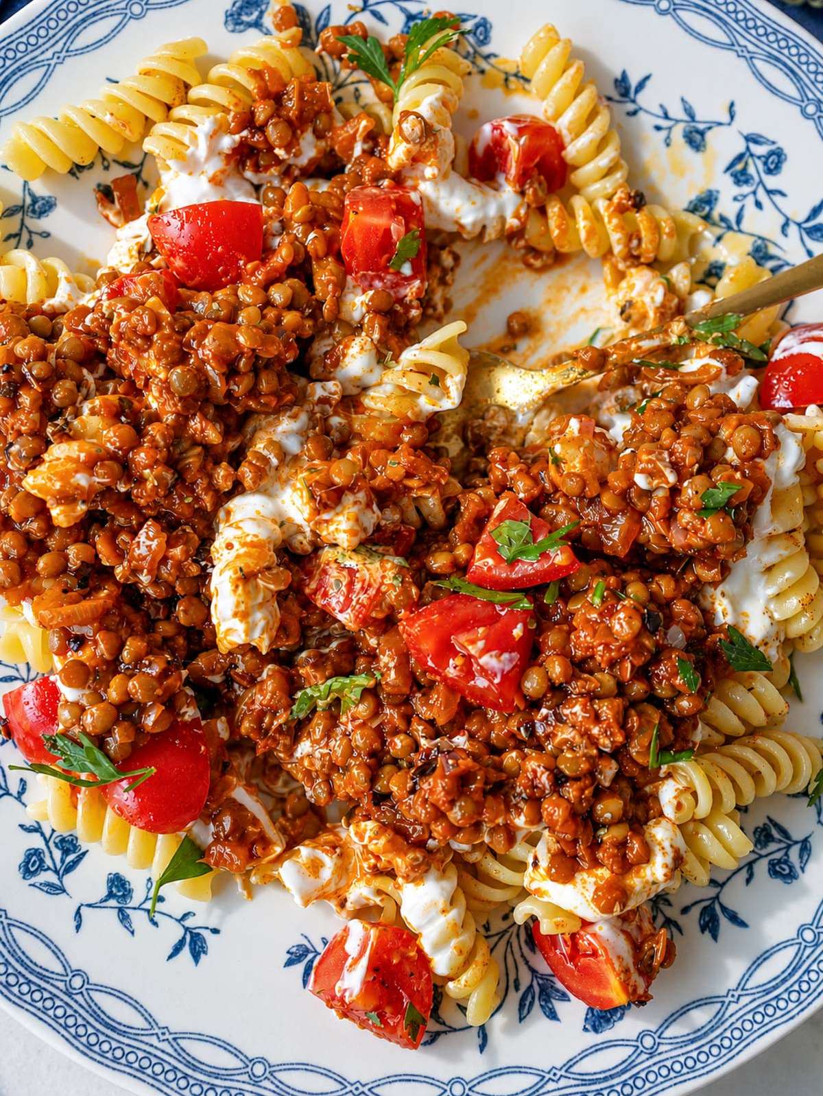 Close-up of glossy spiced lentils over pasta with garlic yogurt and herbs.