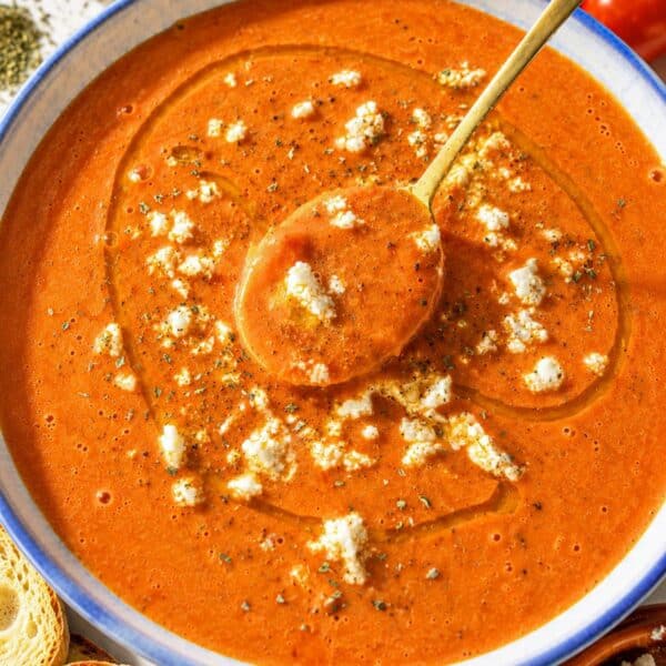 Creamy roasted tomato soup with toasted bread on white marble countertop.