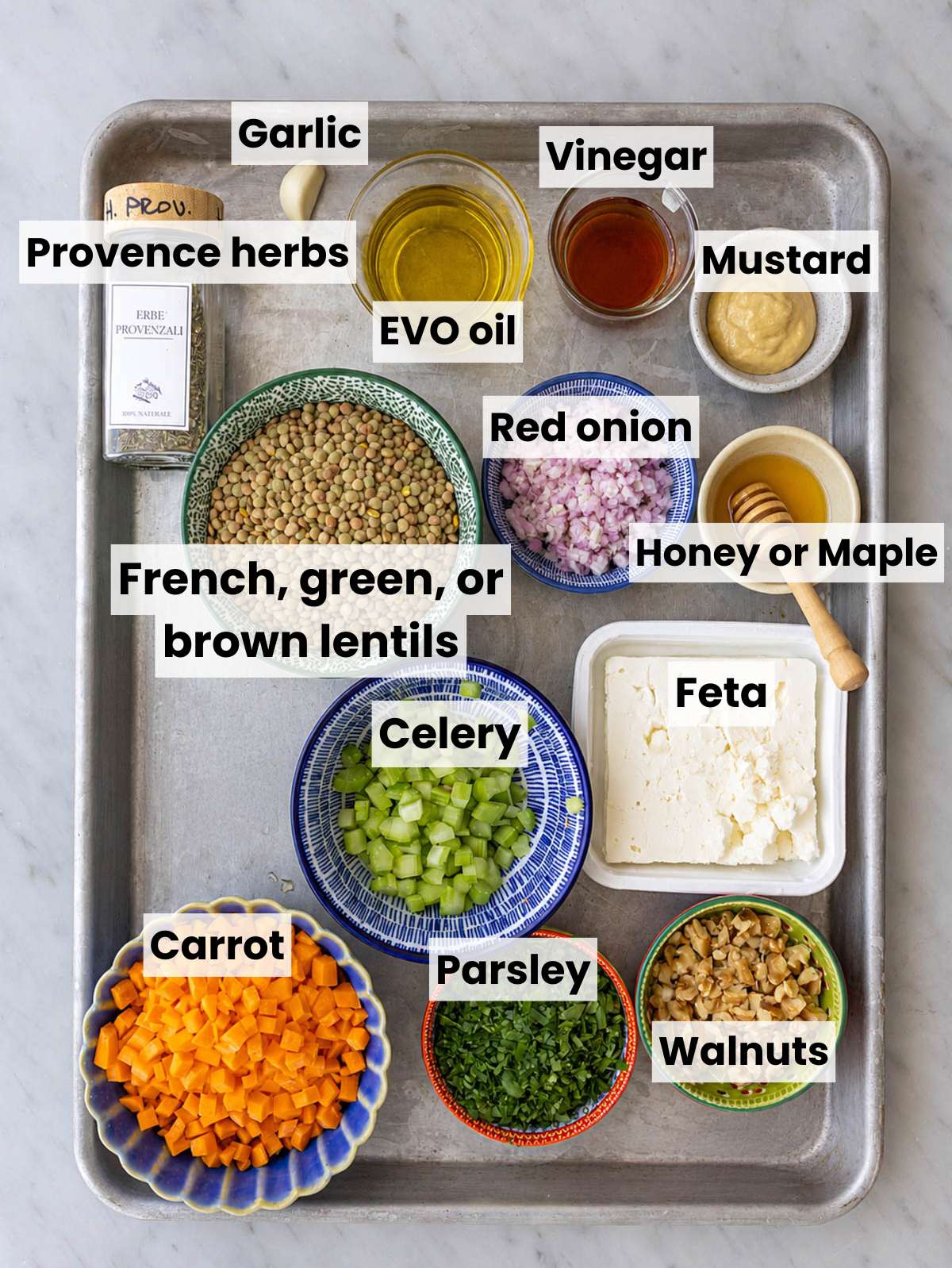 French lentils, vegetables, feta, walnuts, and dressing ingredients on white marble.