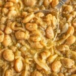 French onion butter beans in a skillet with a silver spoon and bright daylight.